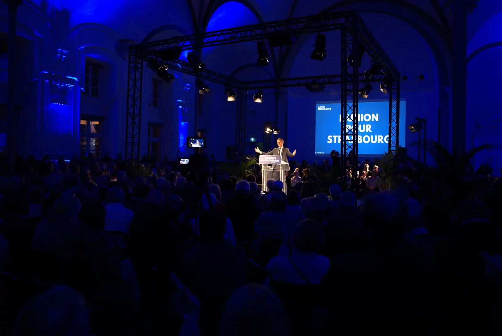 Scène d'un événement éclairée en bleu, filmée depuis le public